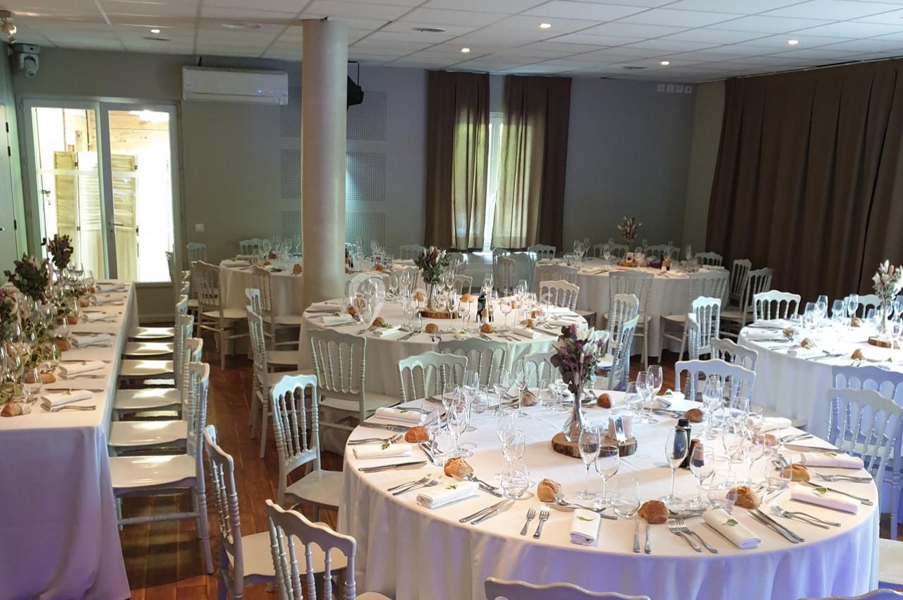 Salle de réception aménagée avec des tables rondes et rectangulaires dressées pour un repas festif.