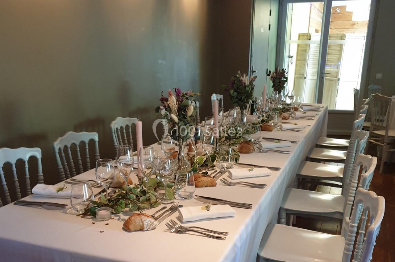 Table dressée pour un repas, avec nappes blanches, couverts, verres, bougies et décorations florales.