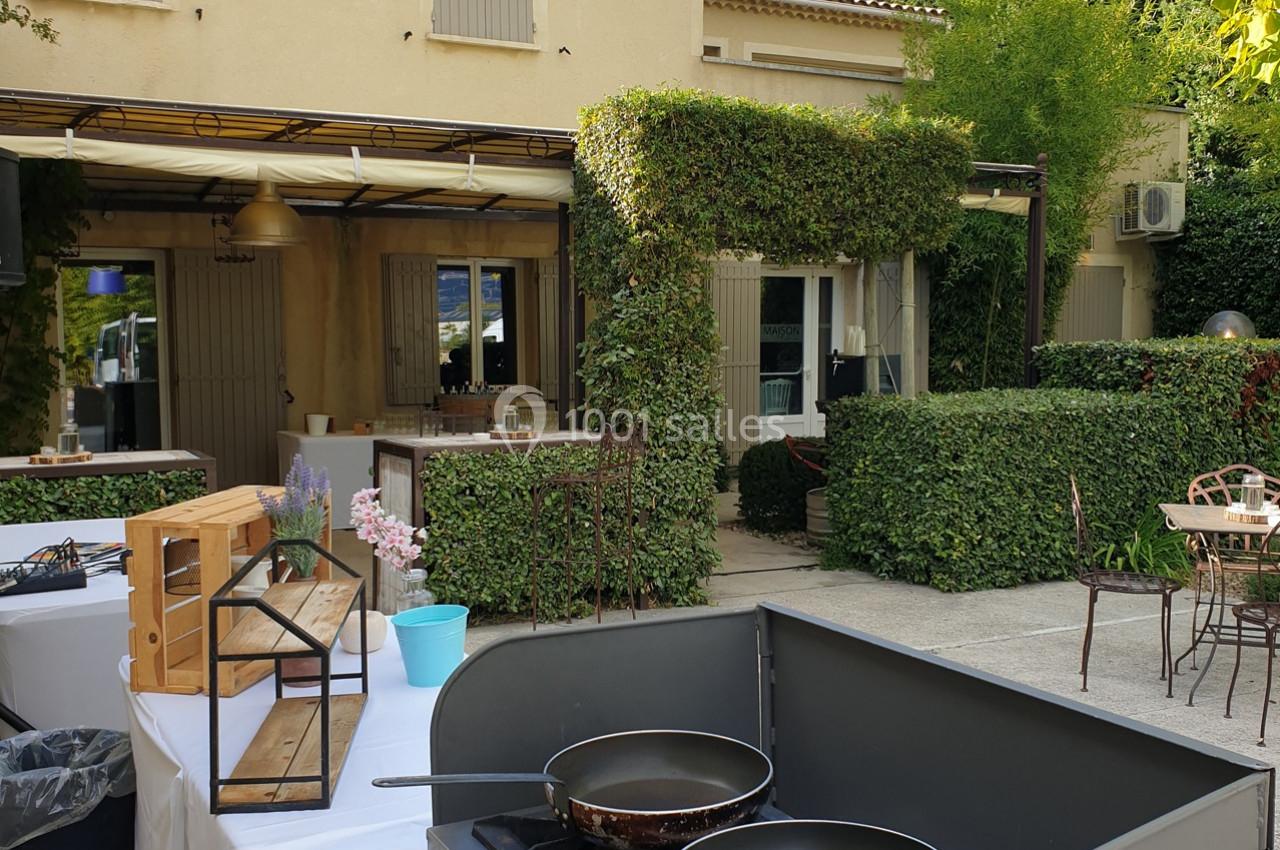 Terrasse extérieure avec tables, chaises, végétation et un espace de cuisine équipé de poêles au premier plan.