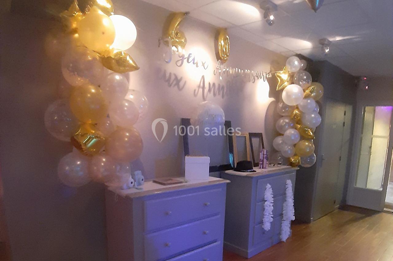 Décoration d'anniversaire avec ballons dorés et blancs, guirlande murale et commodes dans une pièce éclairée.