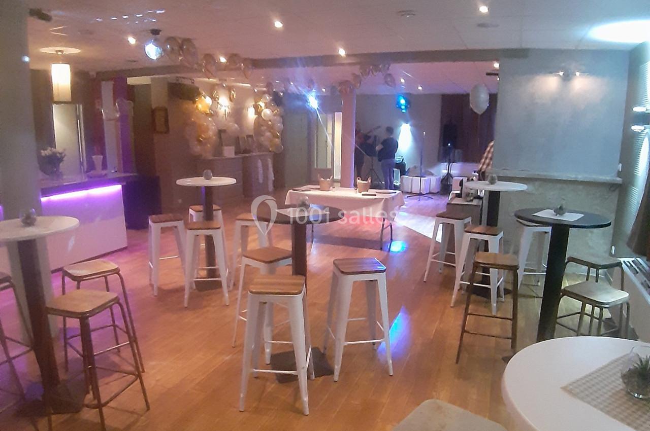 Salle de réception avec tables hautes, tabourets et éclairage tamisé, décorée pour un événement festif.