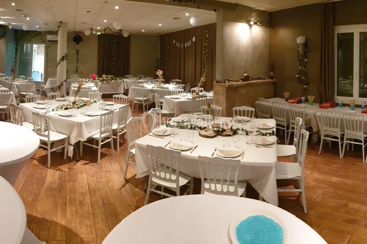 Salle de réception décorée avec des tables dressées, nappes blanches et chaises, prête pour un événement festif.