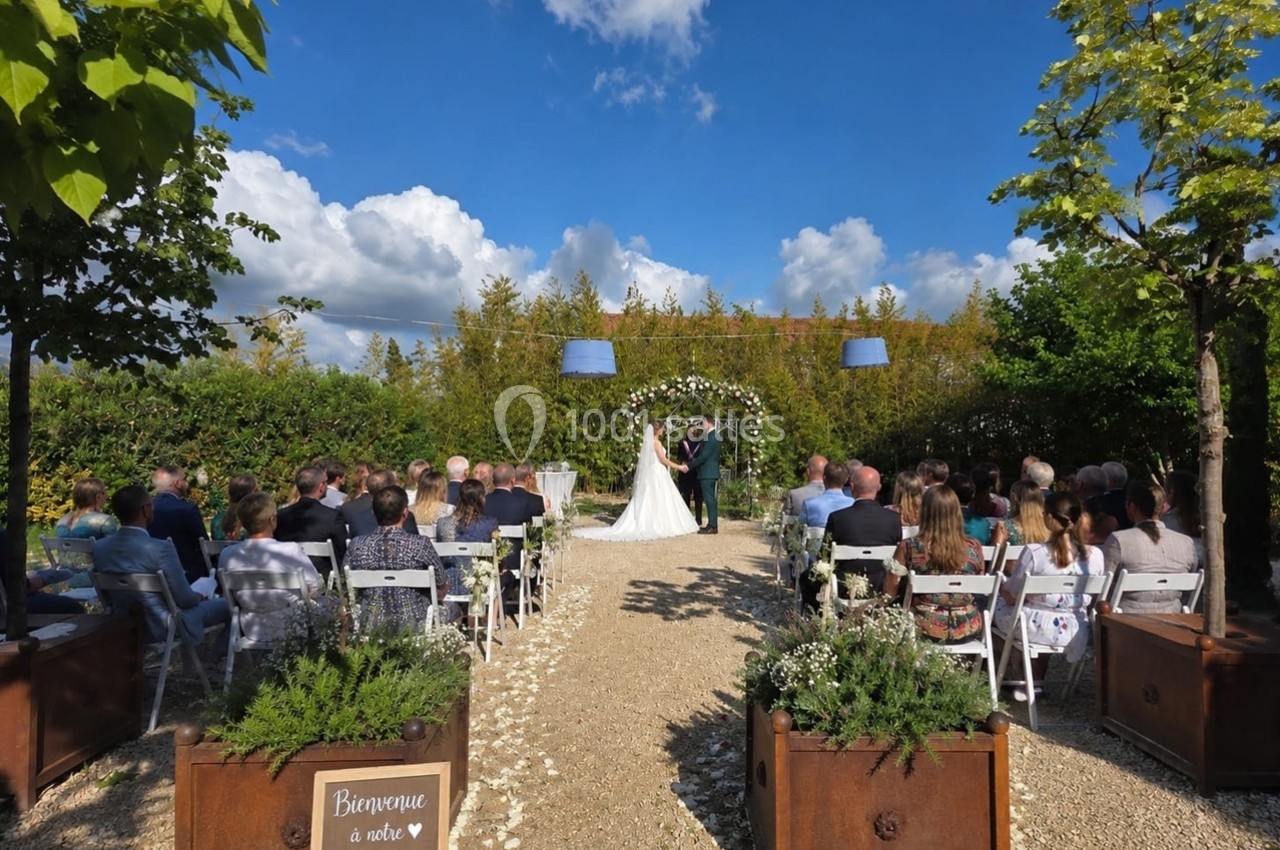 Mariage en extérieur avec des invités assis, un couple échangeant ses vœux sous une arche fleurie.