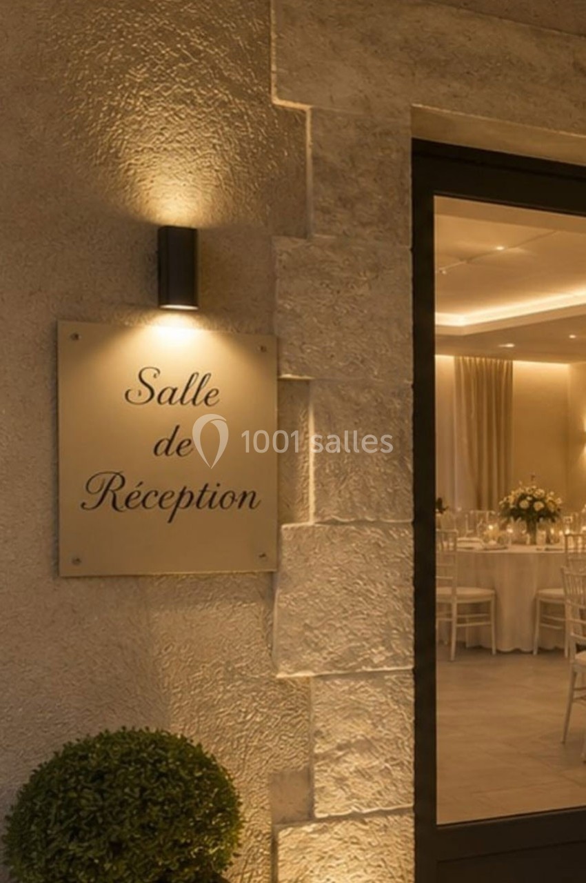 Plaque indiquant ’Salle de Réception’ sur un mur en pierre, avec une porte ouverte laissant voir une salle décorée.