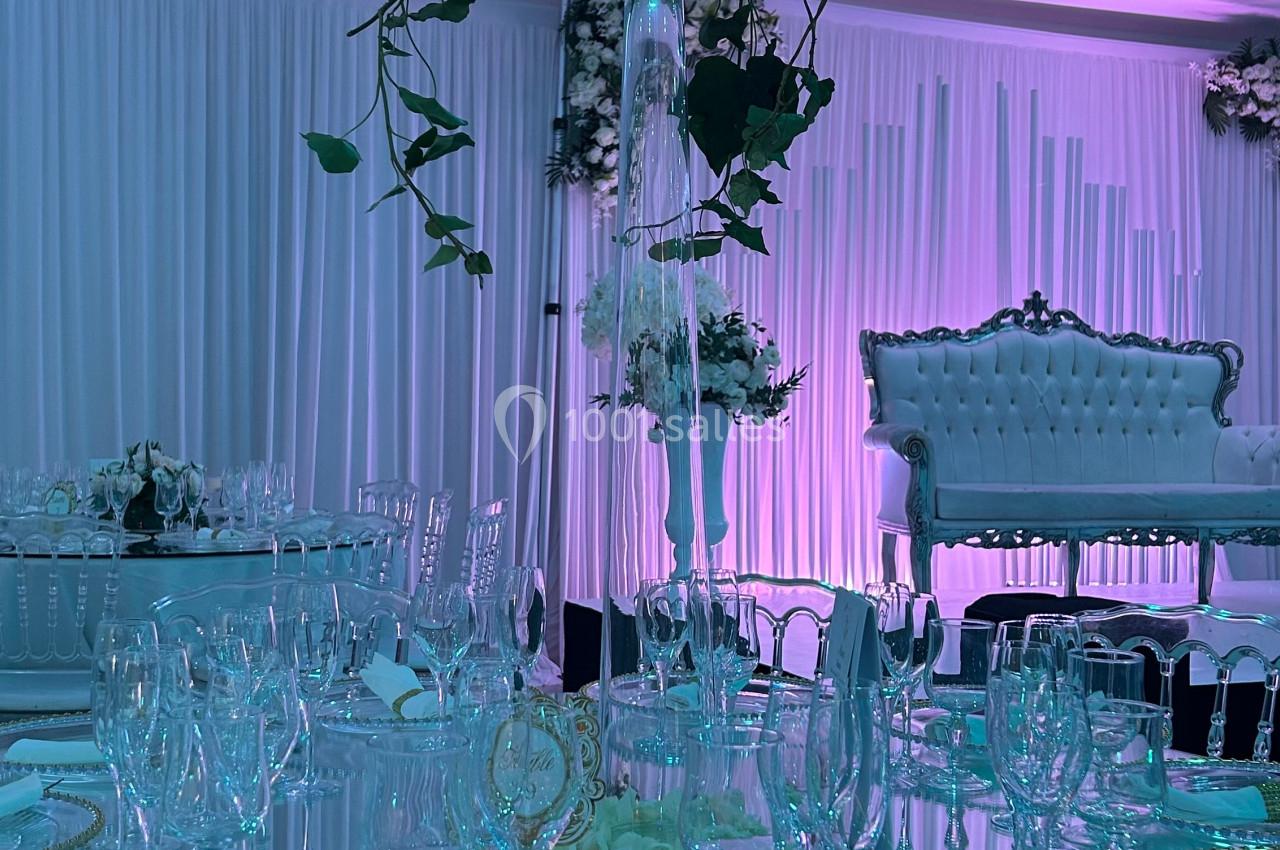 Table de réception élégamment dressée avec vaisselle raffinée, centre de table floral et éclairage tamisé violet.