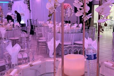 Centre de table décoratif avec bougie, fleurs blanches et roses, entouré de cadeaux sur une table de réception élégante.