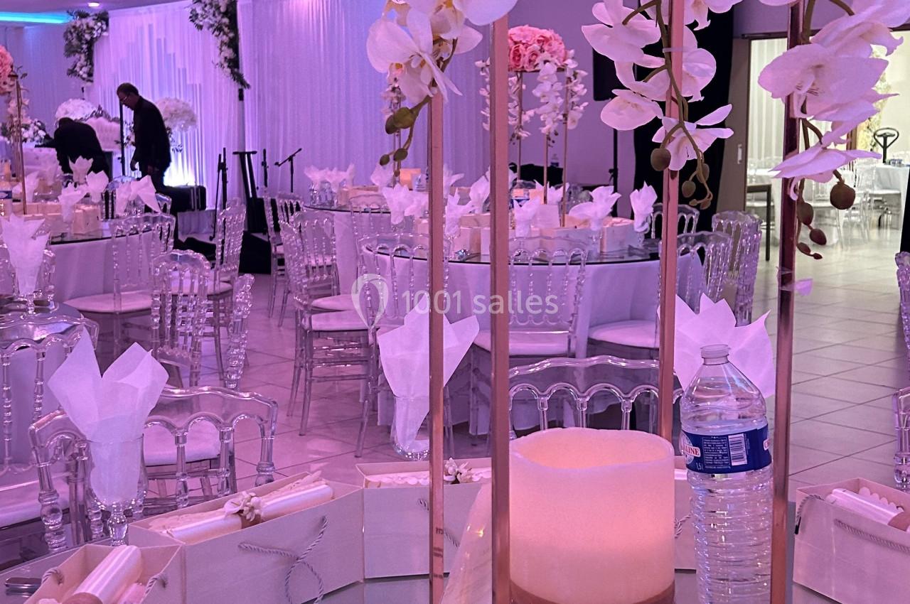 Centre de table décoratif avec bougie, fleurs blanches et roses, entouré de cadeaux sur une table de réception élégante.