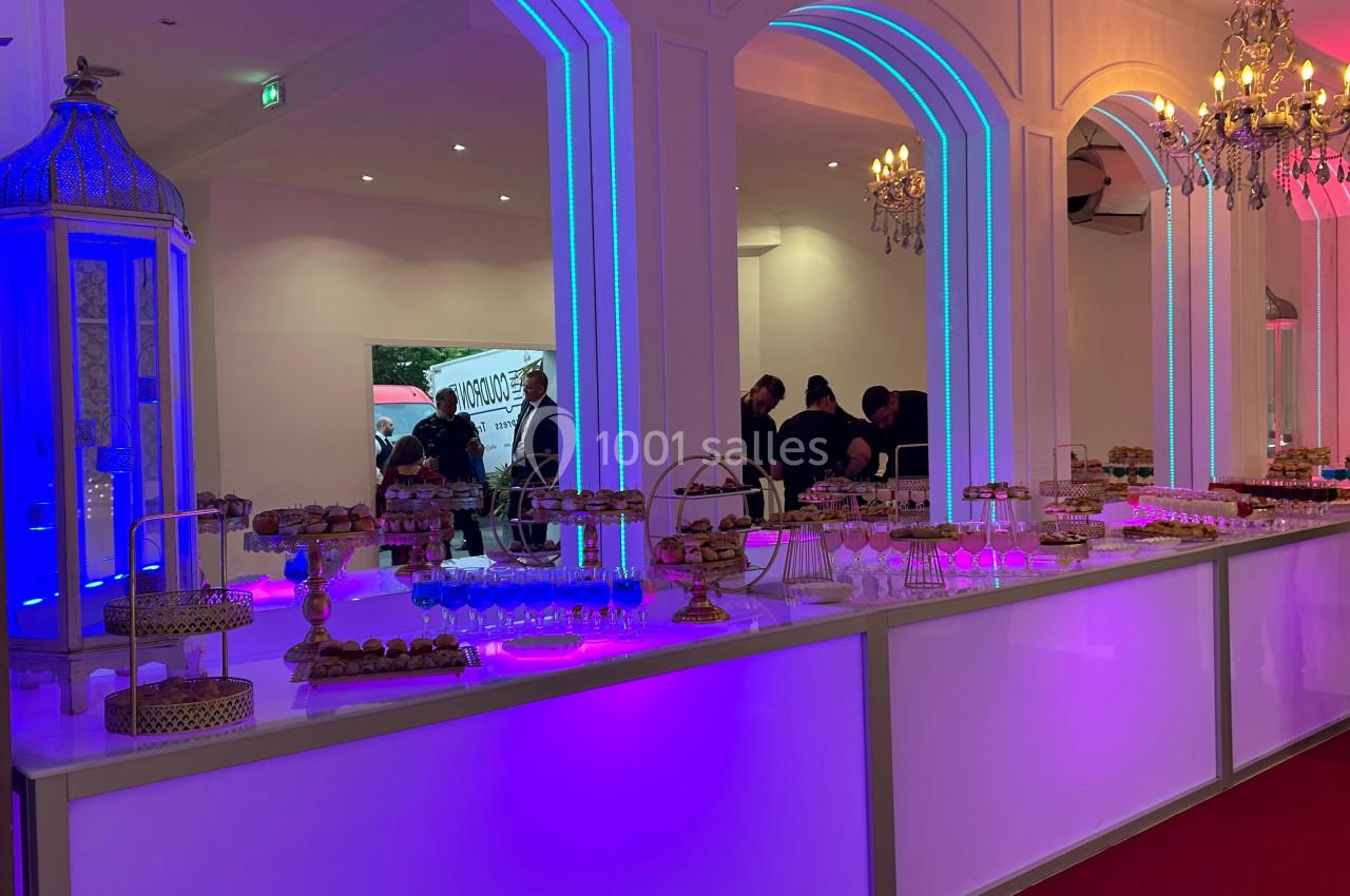 Buffet lumineux avec desserts variés présentés sur des supports élégants dans une salle décorée de lustres et d'arcs…