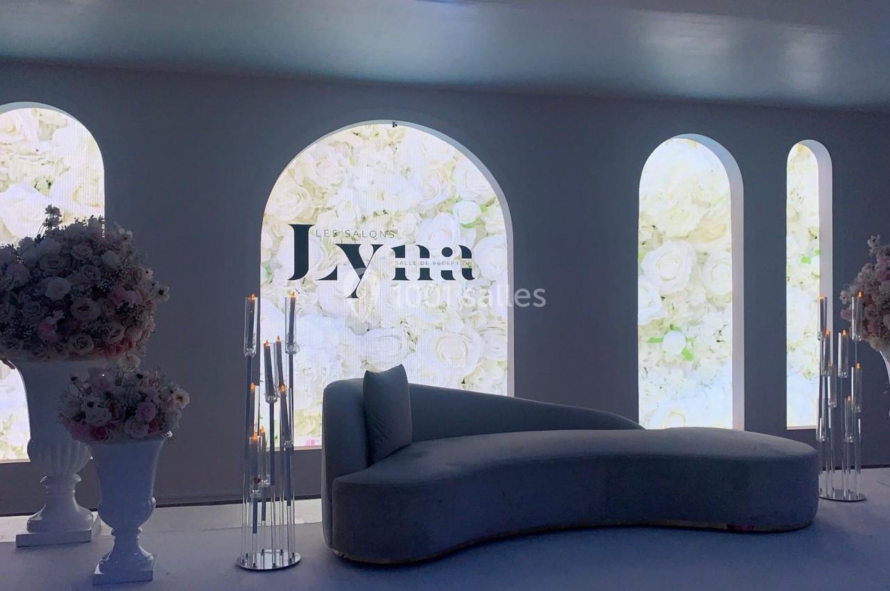 Salon décoré avec un canapé courbé, des arches lumineuses et des compositions florales blanches.