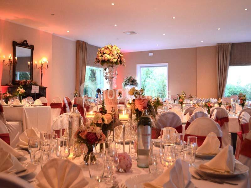 Salle de réception décorée avec des tables dressées, nappes blanches, bouquets de fleurs et chandeliers.