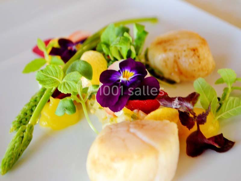 Assiette gastronomique avec noix de Saint-Jacques, asperges, fleurs comestibles et garnitures colorées.