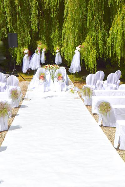Allée centrale blanche décorée pour une cérémonie de mariage en extérieur, entourée de chaises recouvertes de housses…