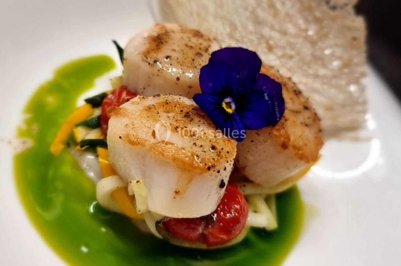 Noix de Saint-Jacques poêlées sur lit de légumes, sauce verte et décorées d'une fleur comestible, accompagnées d'une tuile…