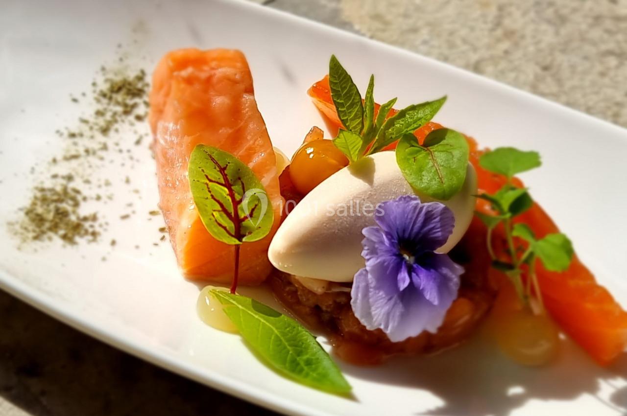 Plat gastronomique avec saumon, mousse blanche, fleurs comestibles et herbes fraîches, présenté sur une assiette blanche.