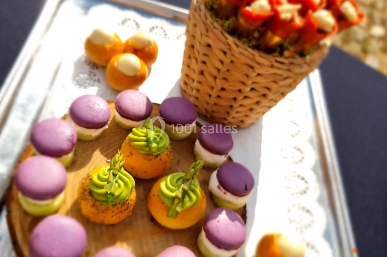 Plateau de pâtisseries colorées avec macarons violets, petits choux garnis et brochettes de fruits dans un panier.