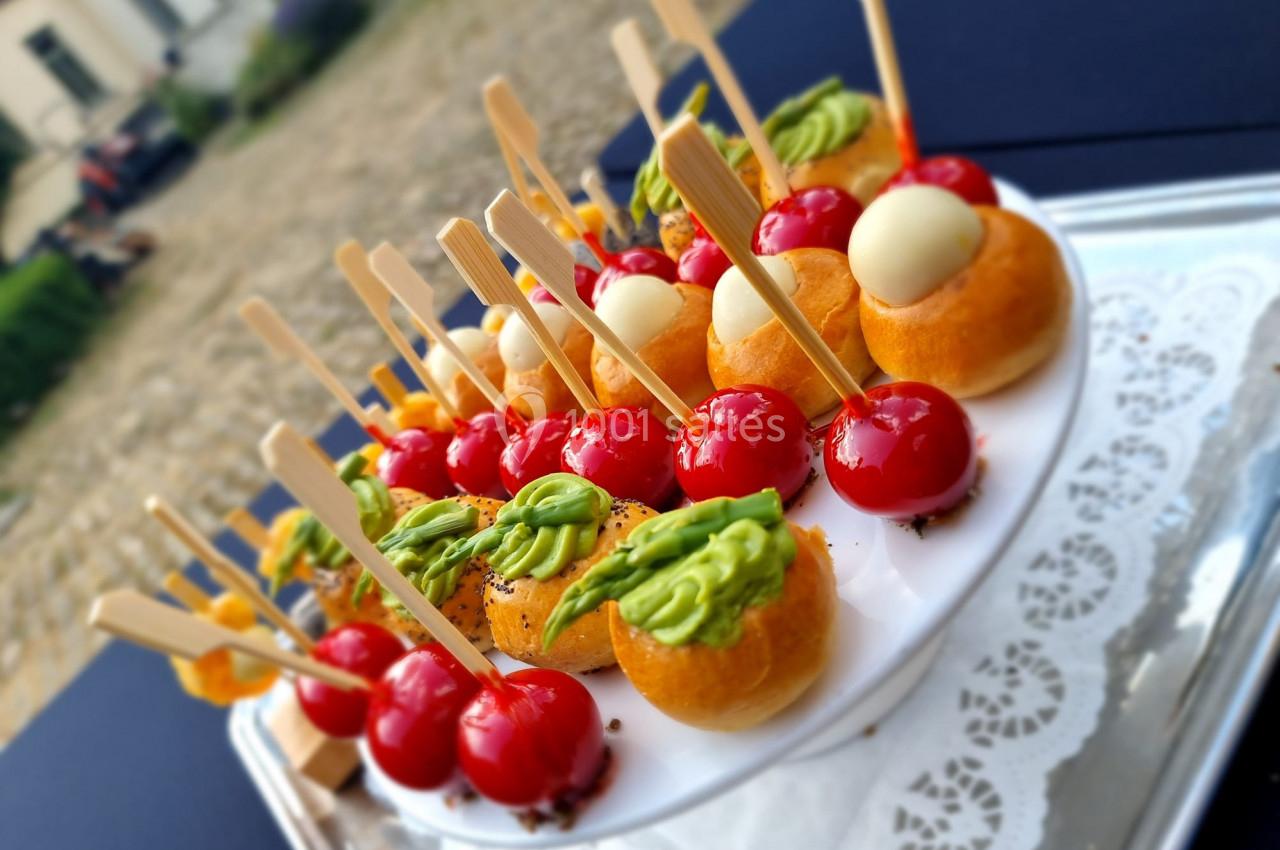 Assortiment de bouchées apéritives colorées sur un plateau, comprenant tomates cerises, choux garnis et brochettes.