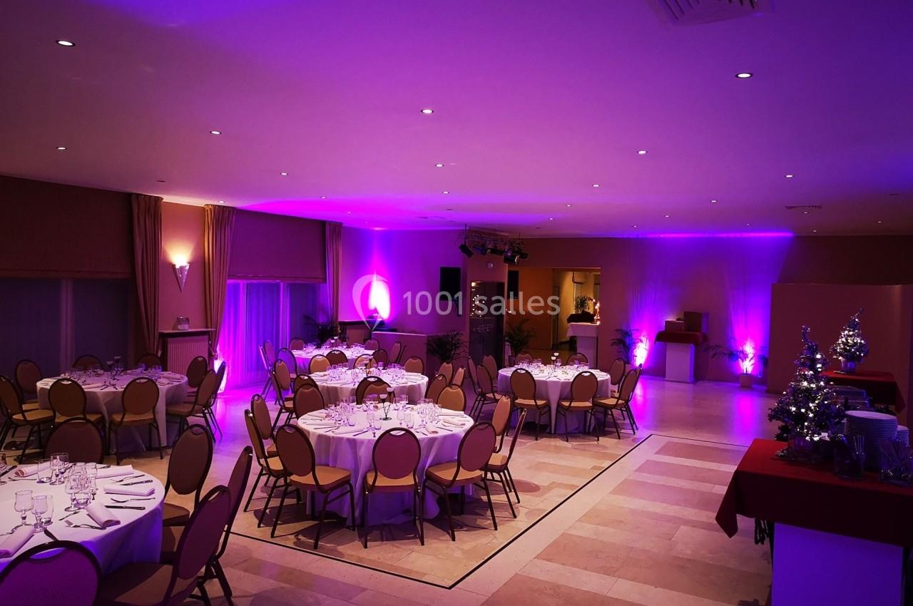 Salle de réception décorée avec des tables rondes dressées, éclairage tamisé et ambiance lumineuse violette.
