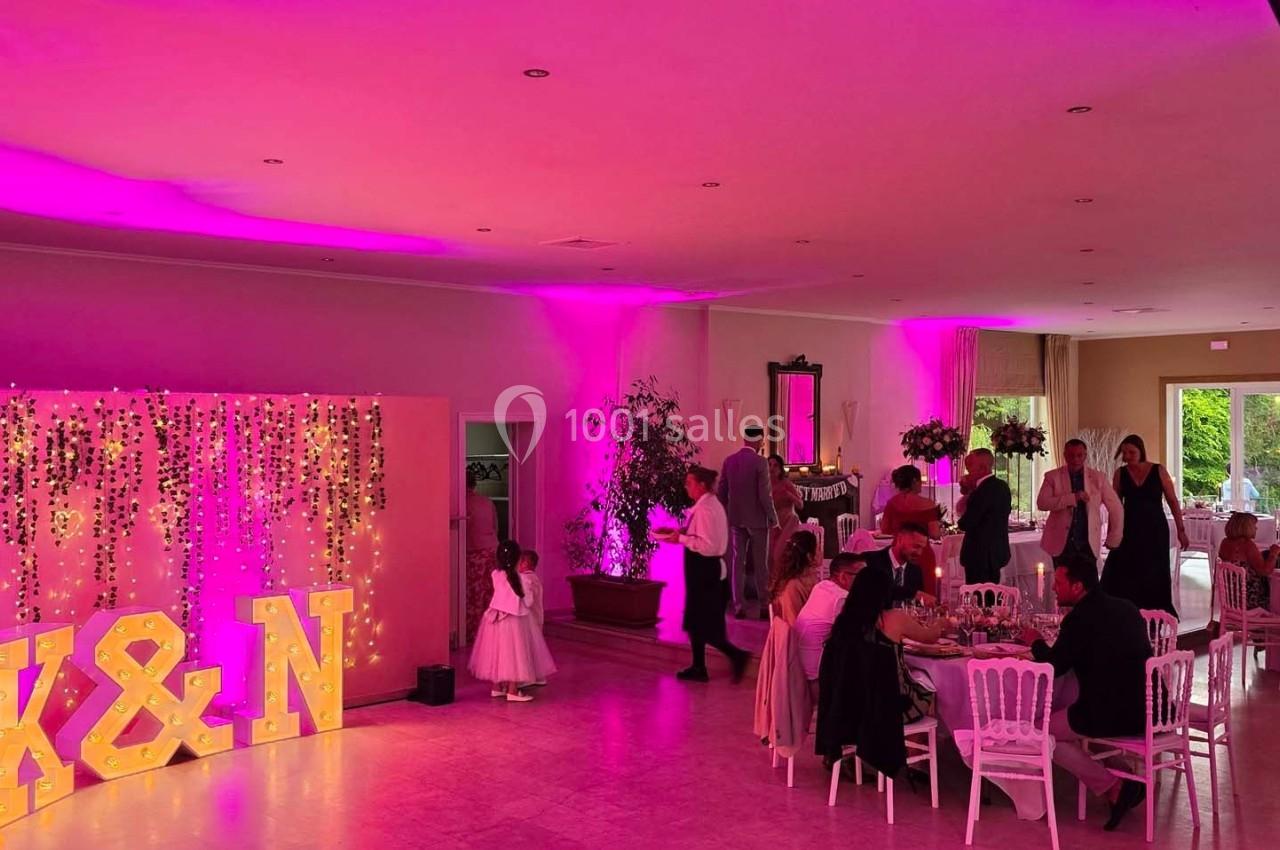 Salle de réception décorée avec des lumières roses, des invités assis et un mur illuminé avec les lettres ’K&N’.