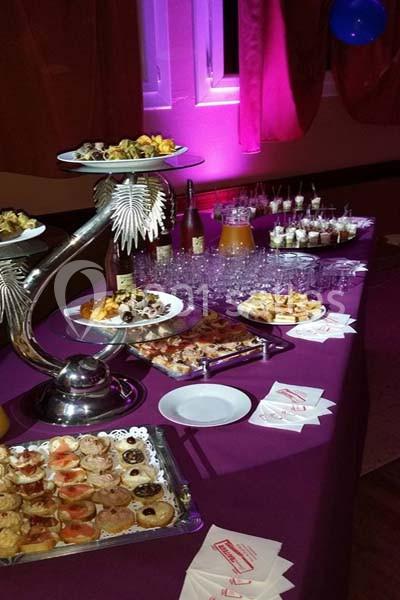 Buffet avec divers plats et desserts disposés sur une table violette, entourée de verres et de boissons.