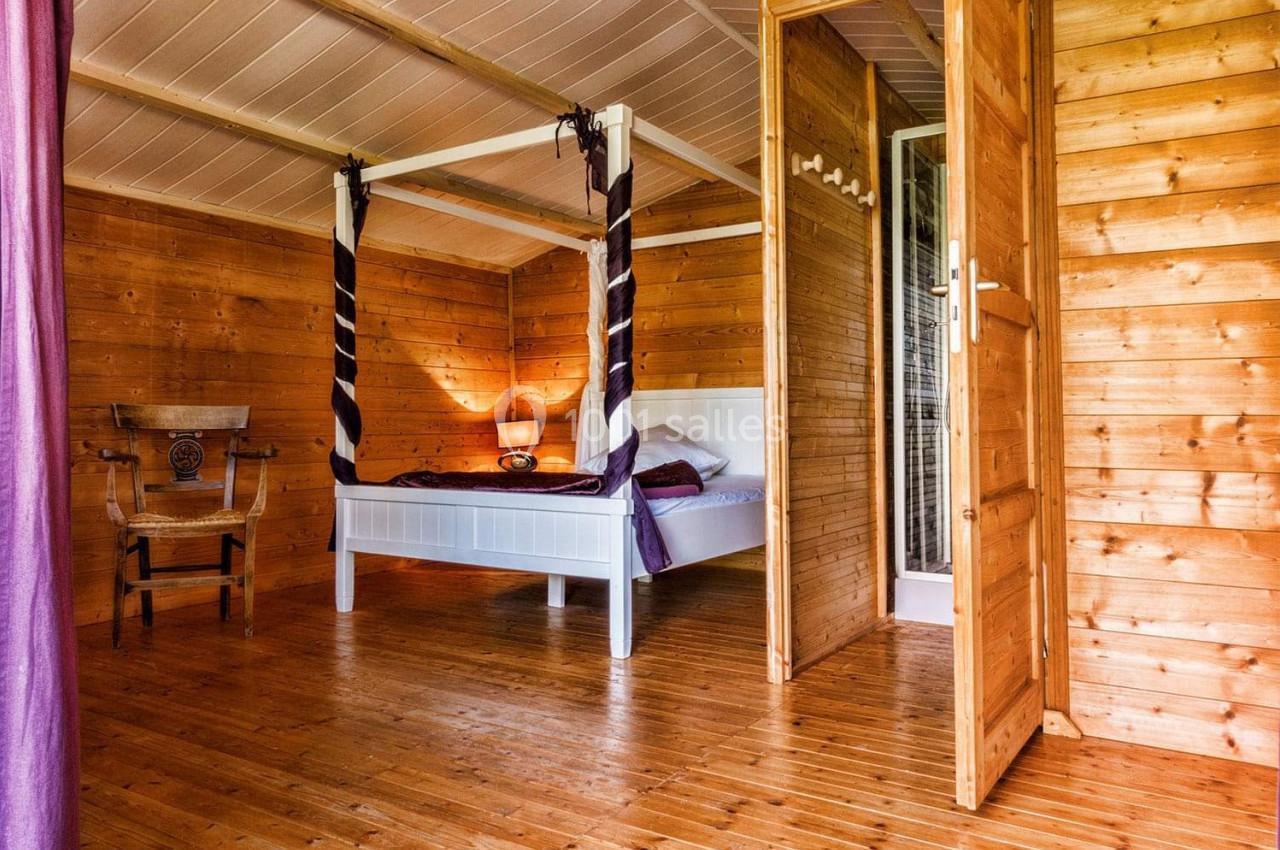 Chambre en bois avec lit à baldaquin blanc, rideaux violets, chaise en bois et lumière douce.