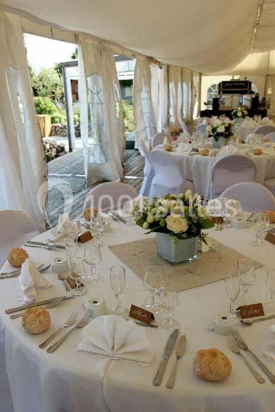 Tables de réception élégamment dressées sous une tente blanche, avec nappes blanches et décorations florales.