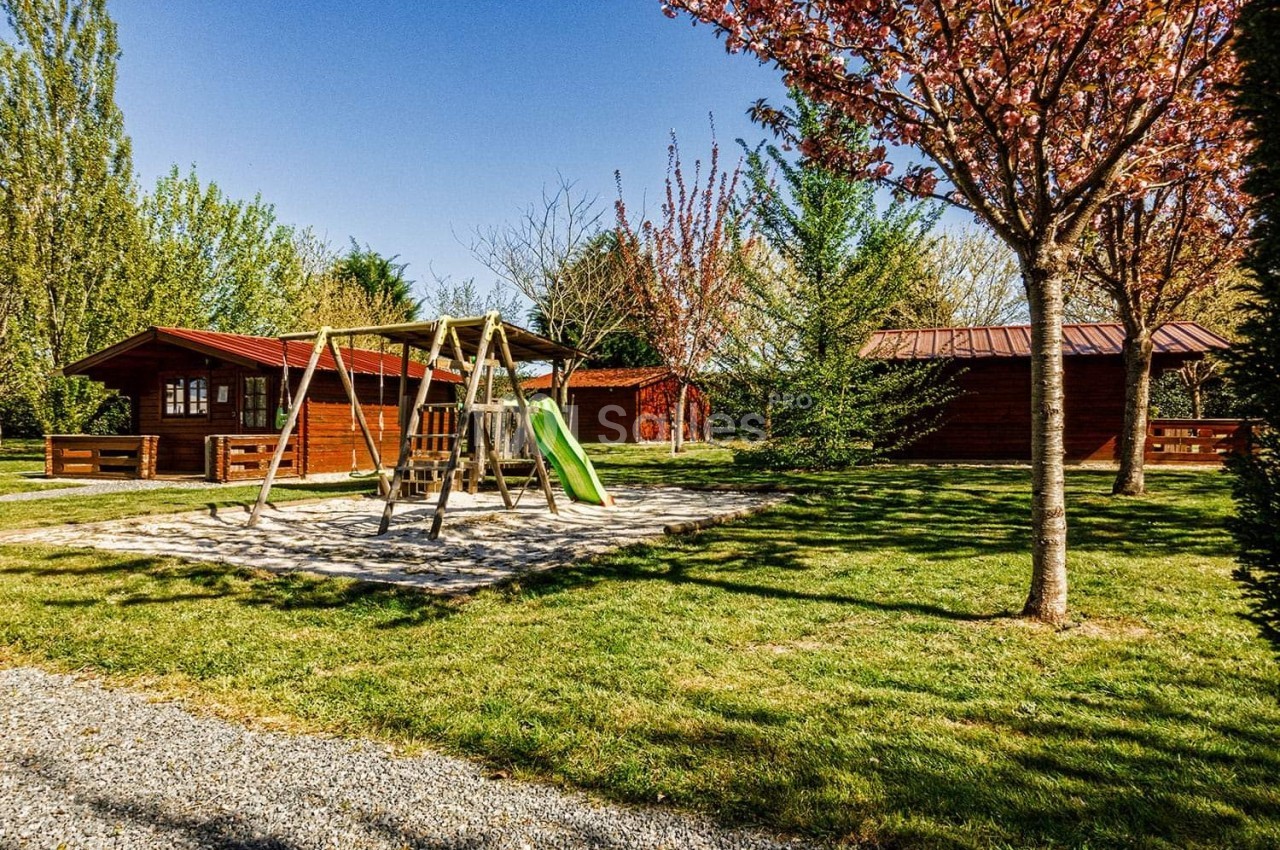 Aire de jeux avec balançoire et toboggan entourée de chalets en bois et d'arbres dans un espace vert.