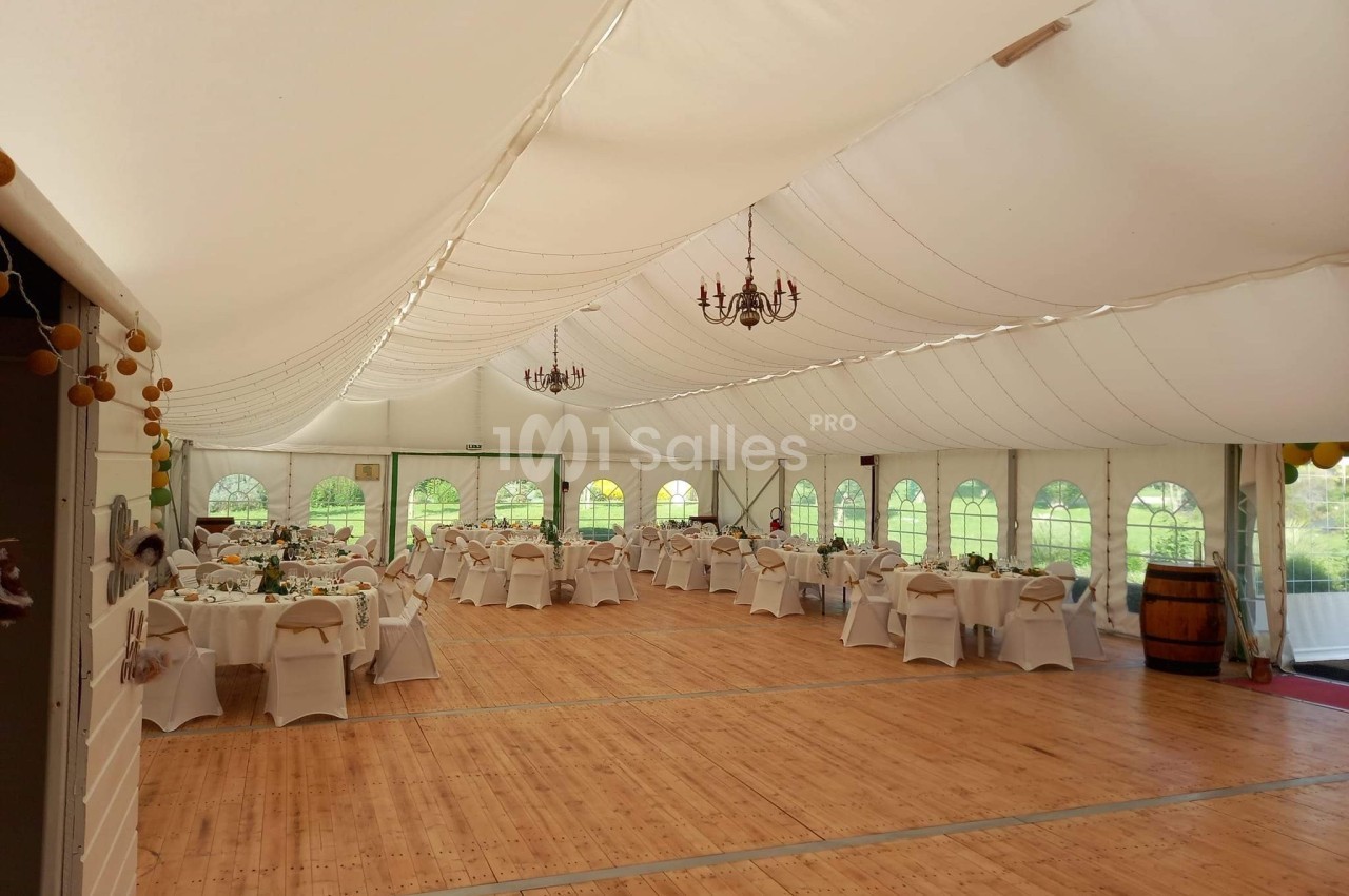 Salle de réception sous chapiteau blanc avec tables dressées, chaises décorées et parquet en bois.