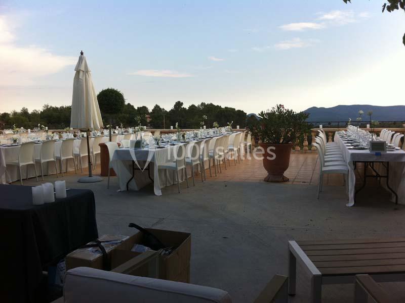 Tables dressées en extérieur pour un événement, avec nappes blanches, chaises alignées et vue sur des collines.