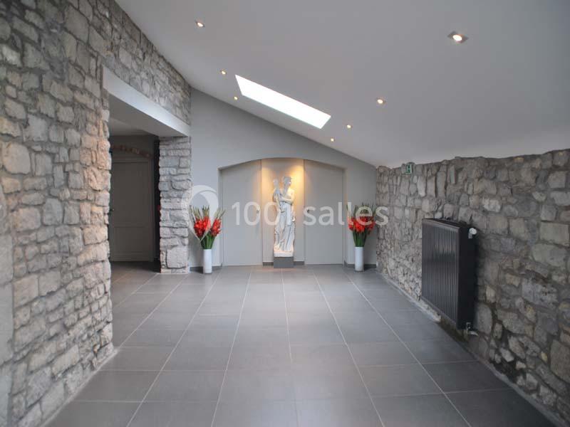 Location salle Ciney (Province de Namur) - Le Domaine d'Achêne #11 Couloir en pierre avec sol en carrelage gris, statue blanche au fond, éclairage encastré et plantes décoratives.