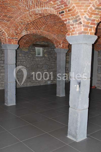 Location salle Ciney (Province de Namur) - Le Domaine d'Achêne #19 Voûte en briques rouges avec piliers en pierre, sol carrelé gris et mur en pierre apparente.