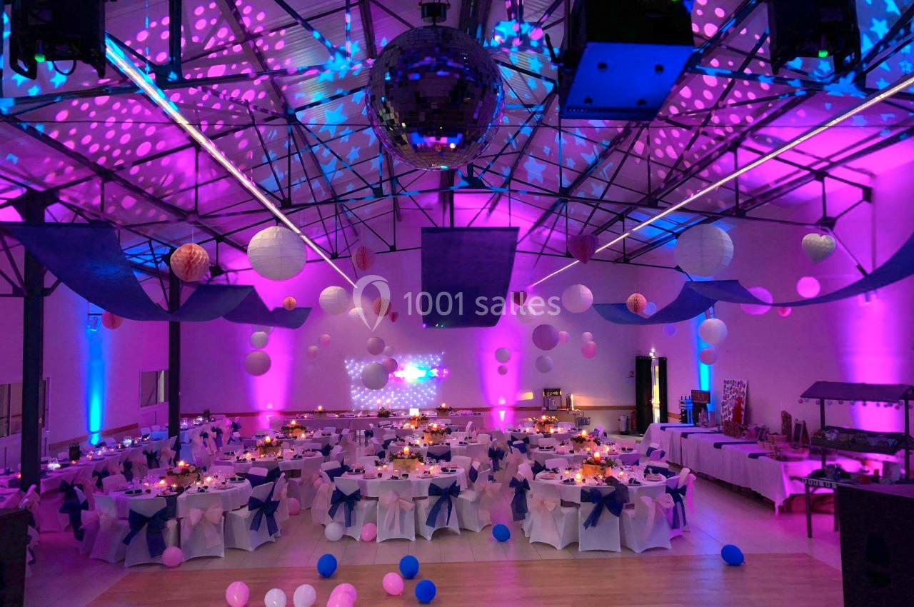 Salle de réception décorée avec des guirlandes lumineuses, des ballons et des tables dressées pour un événement festif.