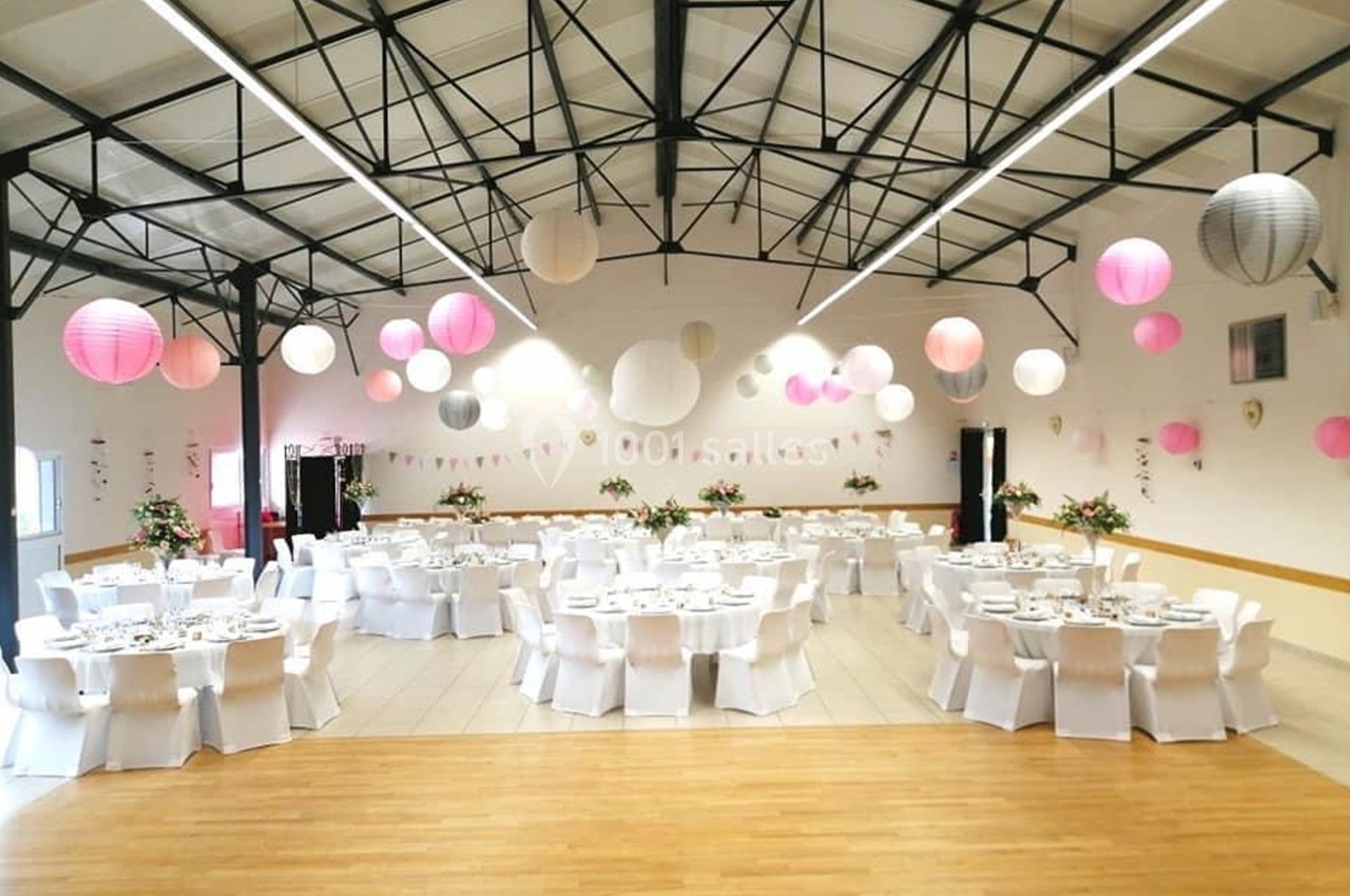 Salle de réception décorée avec des lanternes suspendues et des tables rondes dressées avec nappes blanches.