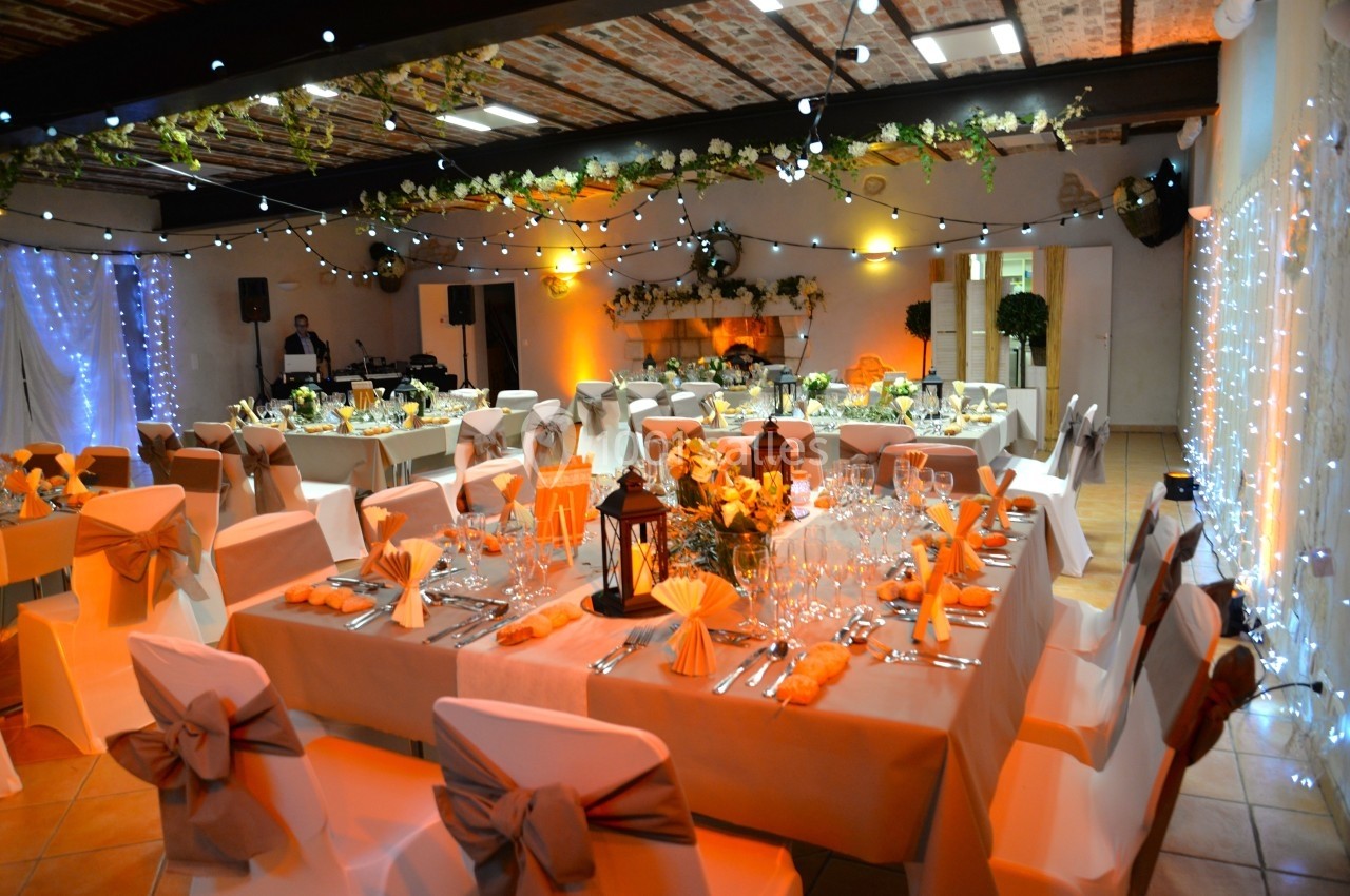 Salle de réception décorée avec des guirlandes lumineuses, des tables dressées et des chaises ornées de nœuds.