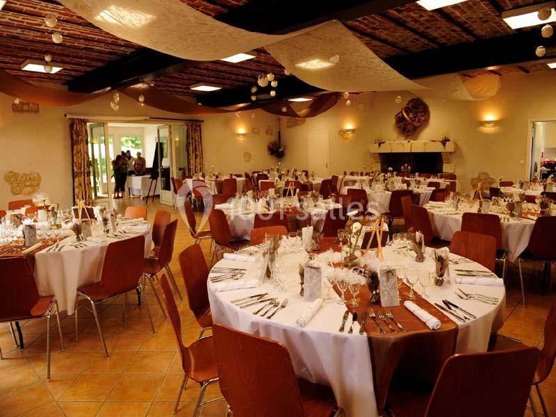 Salle de réception décorée avec des tables rondes dressées pour un événement, éclairée par une lumière chaleureuse.