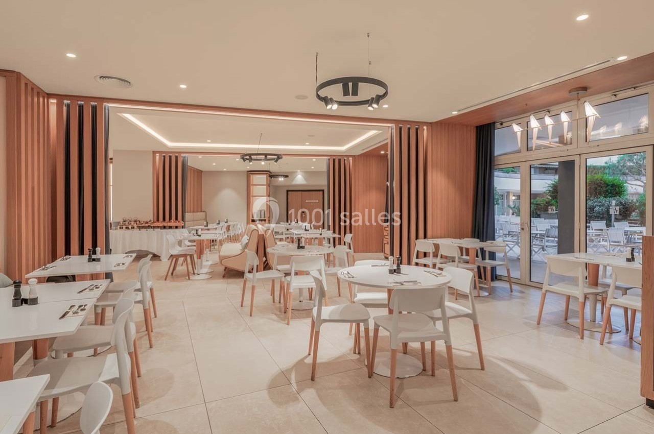 Salle de restaurant lumineuse avec des tables rondes, des chaises blanches et une vue sur une terrasse extérieure.