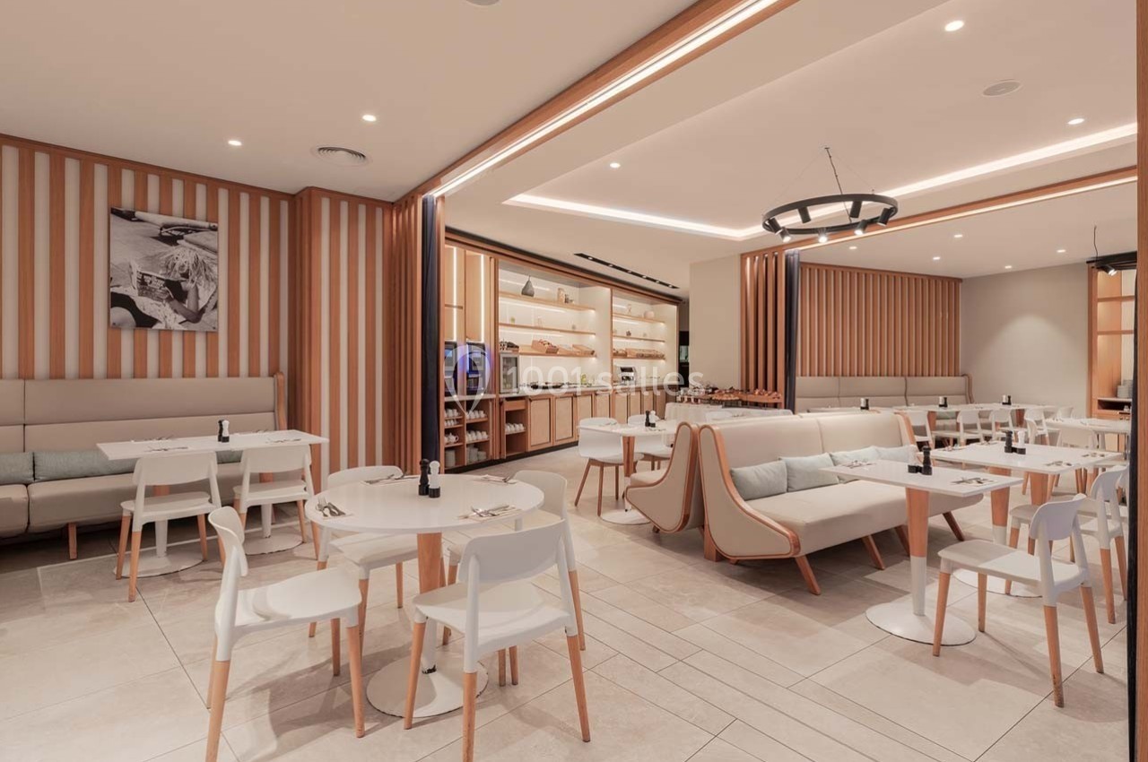 Salle de restaurant moderne avec mobilier clair, tables dressées et éclairage chaleureux.