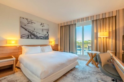 Miniature Location salle Saint-Laurent-du-Var (Alpes-Maritimes) - Playamesa #42 Chambre d'hôtel lumineuse avec lit double, bureau, fauteuil, grandes fenêtres et vue sur un balcon.