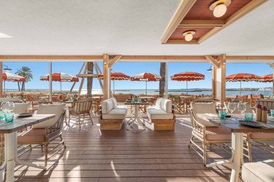 Miniature Location salle Saint-Laurent-du-Var (Alpes-Maritimes) - Playamesa #3 Balcon avec table et chaises blanches, vue sur des palmiers, la mer et un ciel bleu, sous un toit en panneaux blancs.