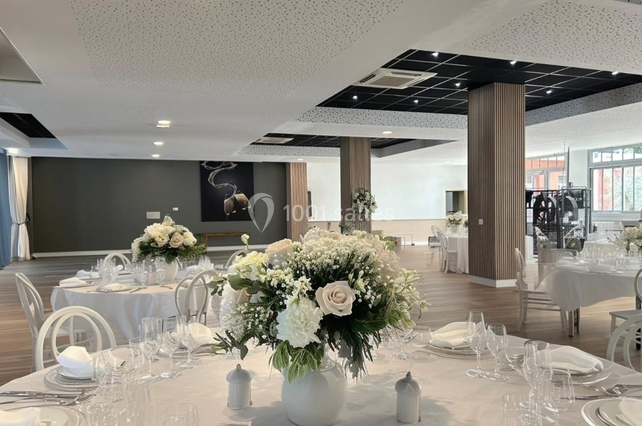 Salle de réception élégante avec tables dressées, décorées de bouquets de fleurs blanches et ambiance lumineuse.