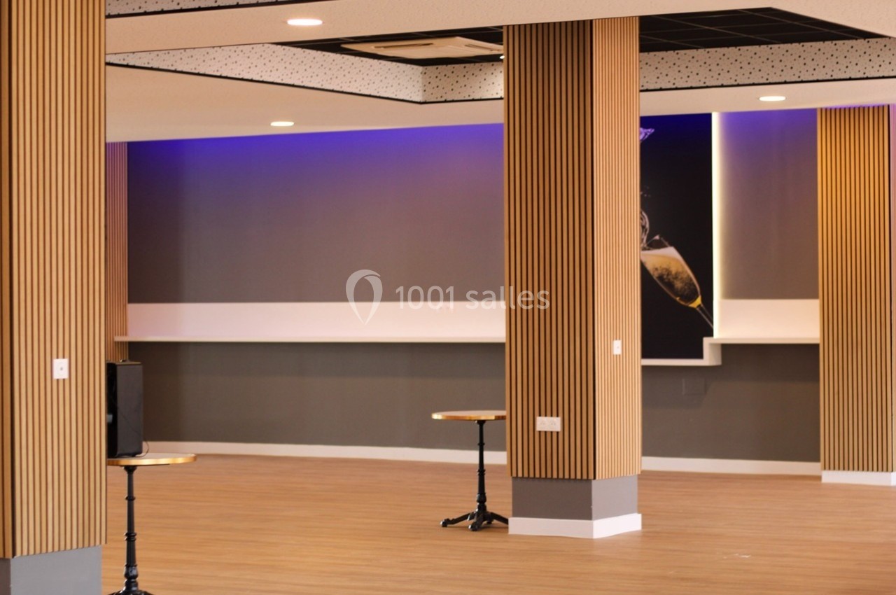 Salle vide avec parquet clair, colonnes en bois, murs gris et éclairage LED violet au plafond.