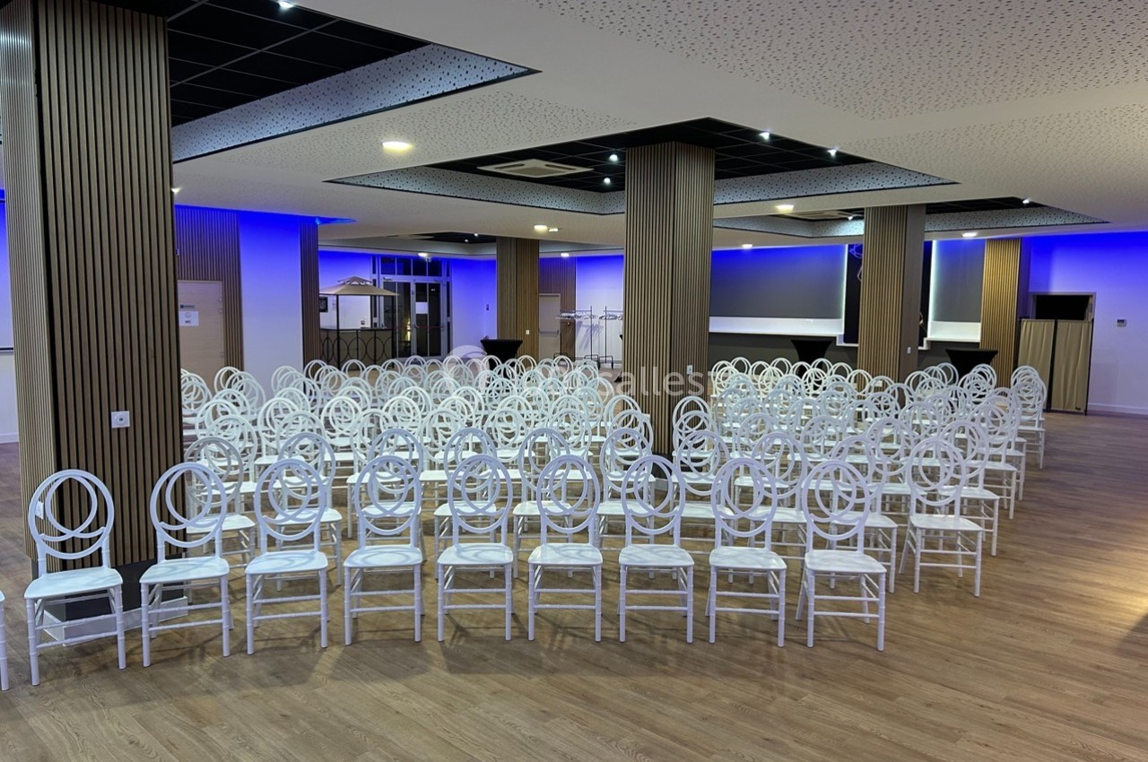 Salle de conférence moderne avec des rangées de chaises blanches alignées sur un sol en bois.