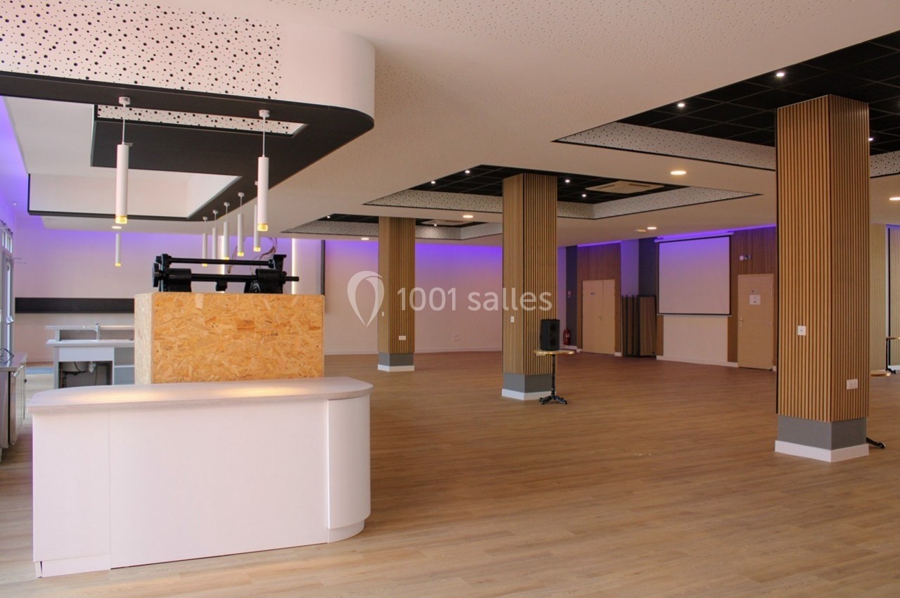 Salle spacieuse avec parquet clair, éclairage LED violet, colonnes en bois et comptoir blanc moderne.