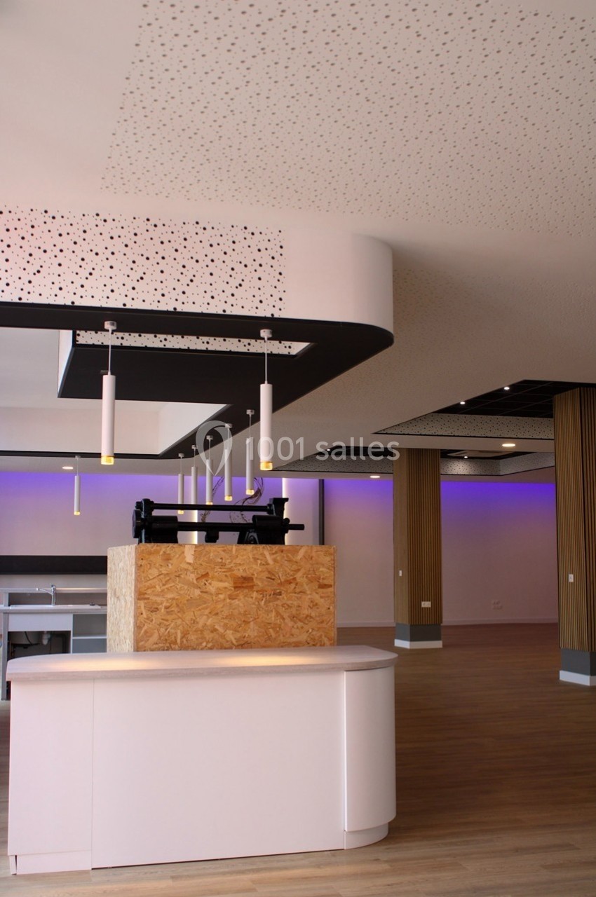 Intérieur moderne avec comptoir en bois, éclairage suspendu et plafond perforé, ambiance lumineuse et épurée.