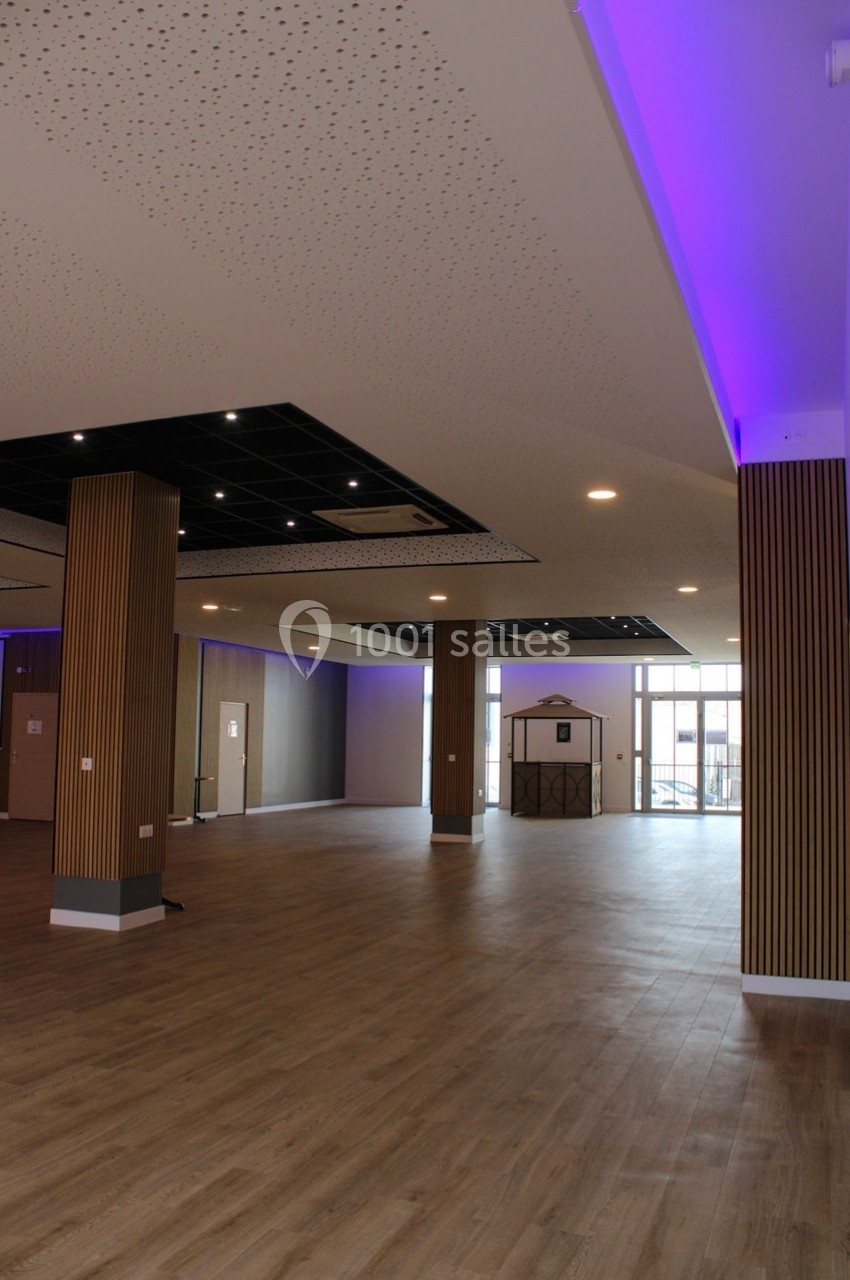 Salle spacieuse avec parquet, colonnes en bois, plafond perforé et éclairage LED violet.