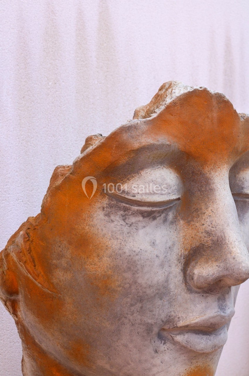 Fragment de sculpture en pierre représentant un visage humain avec une expression sereine, partiellement érodé.