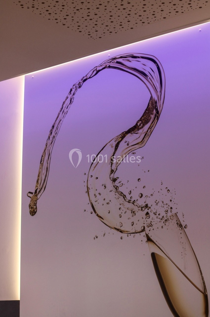 Projection artistique d'un verre de vin blanc éclaboussant, éclairé par une lumière violette sur un mur.