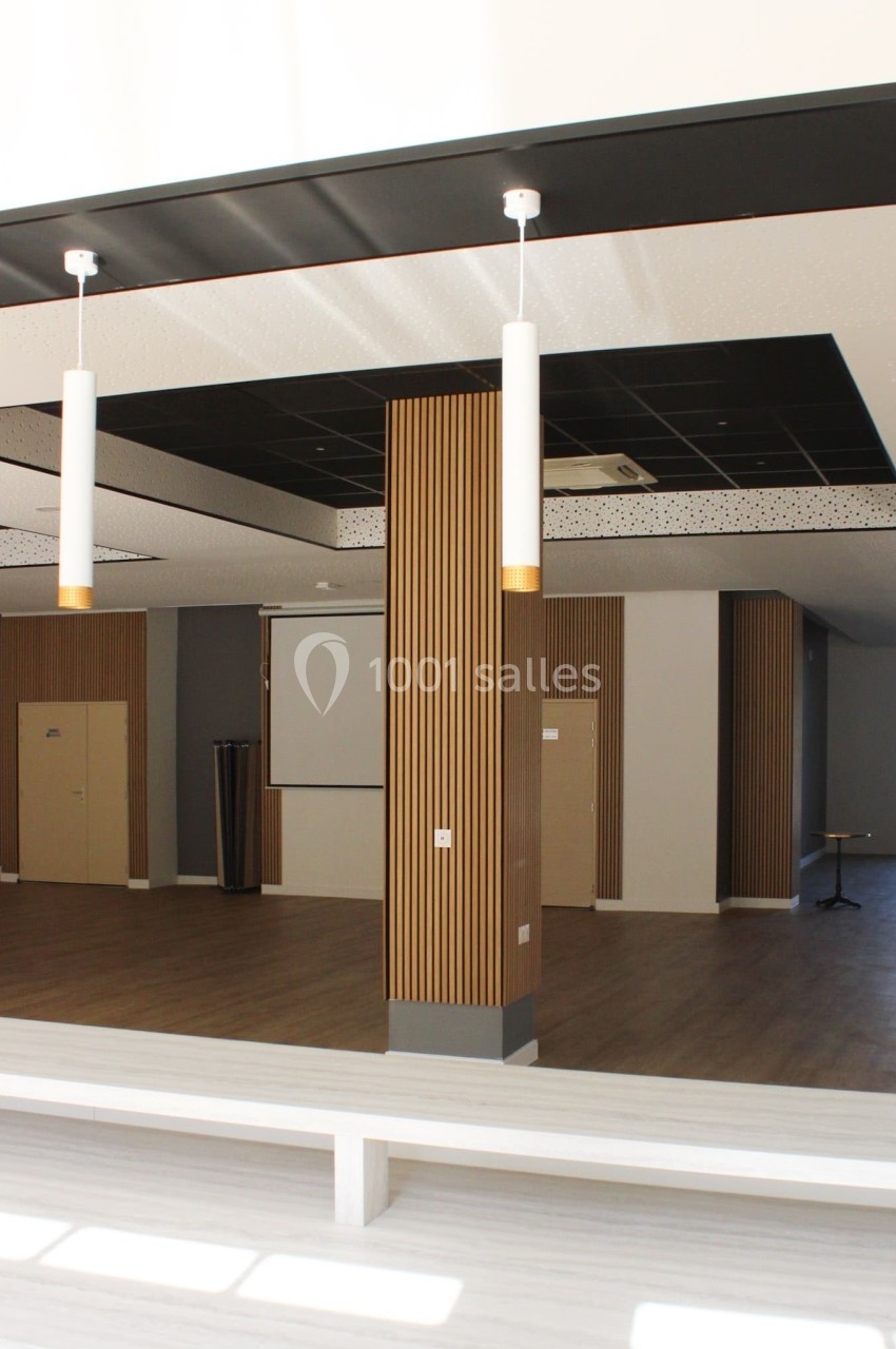 Salle moderne avec parquet, murs clairs, panneaux en bois vertical, plafond noir et éclairage suspendu.