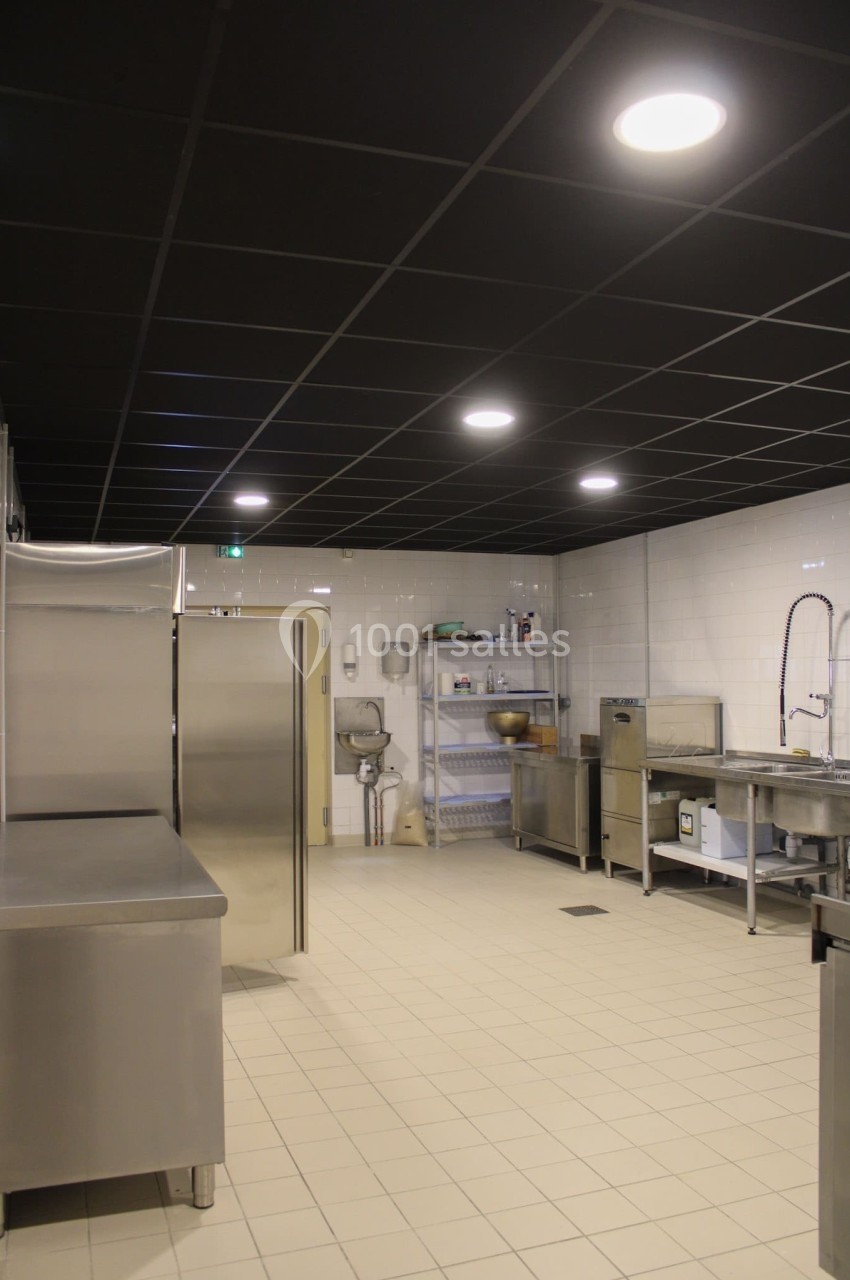 Cuisine professionnelle avec équipements en inox, carrelage clair au sol, murs blancs et éclairage au plafond noir.