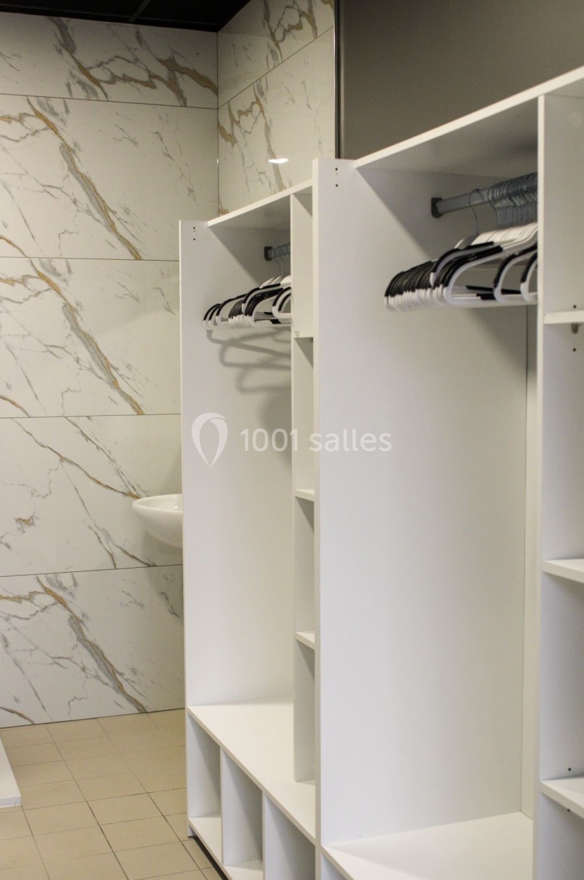 Vestiaire moderne avec casiers blancs ouverts, cintres suspendus et murs en carrelage effet marbre.