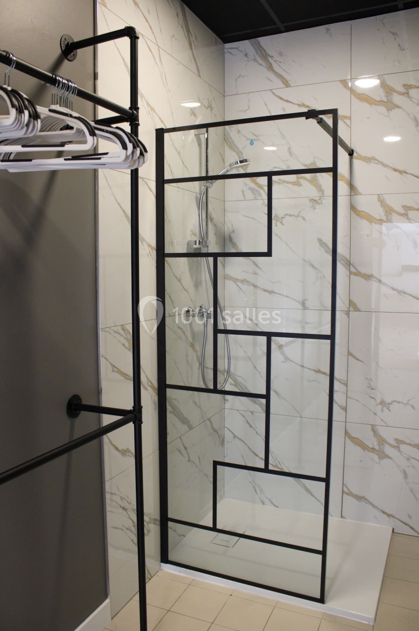Douche moderne avec paroi en verre à motifs géométriques noirs, entourée de murs en carrelage effet marbre.